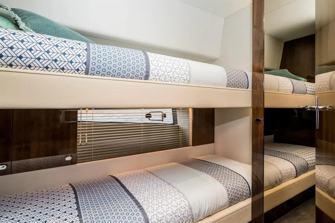 Bunk beds with patterned bedding in a modern interior, featuring a mirrored wardrobe and window blinds.